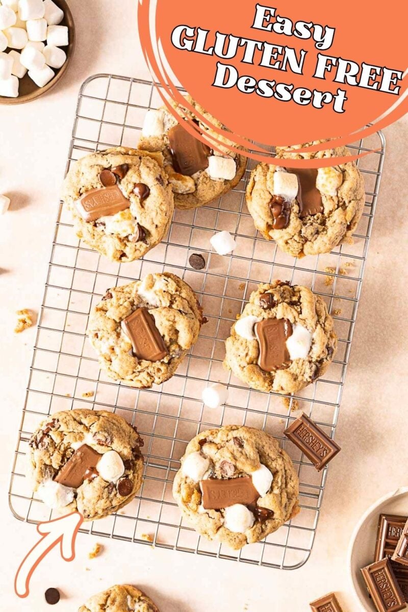 Cookies with chocolate pieces and mini marshmallows cooling on a wire rack, with text overlay reading “Easy GLUTEN FREE Dessert.” These delicious S’Mores Cookies are the perfect gluten free treat for any occasion.