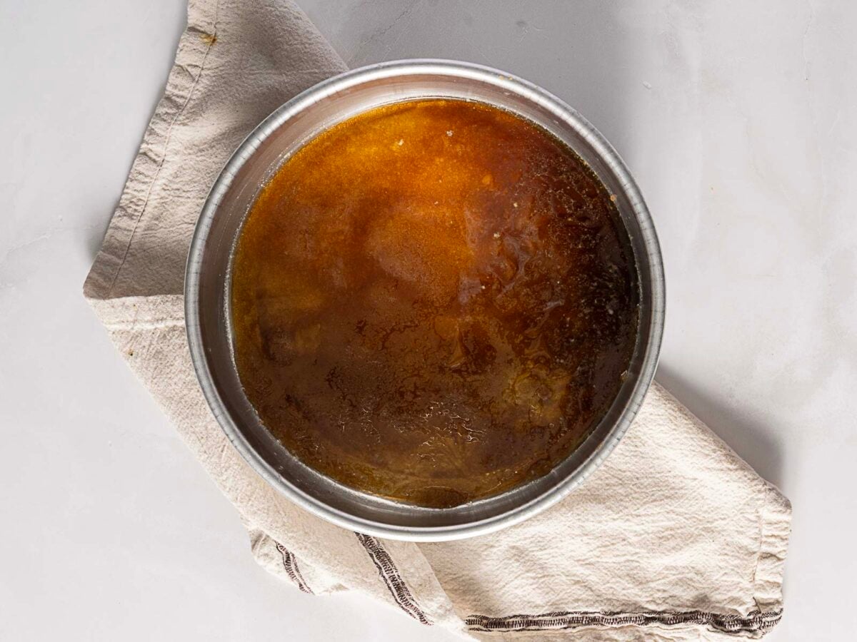 A metal bowl filled with brown liquid sits on a folded beige cloth atop a light-colored surface.