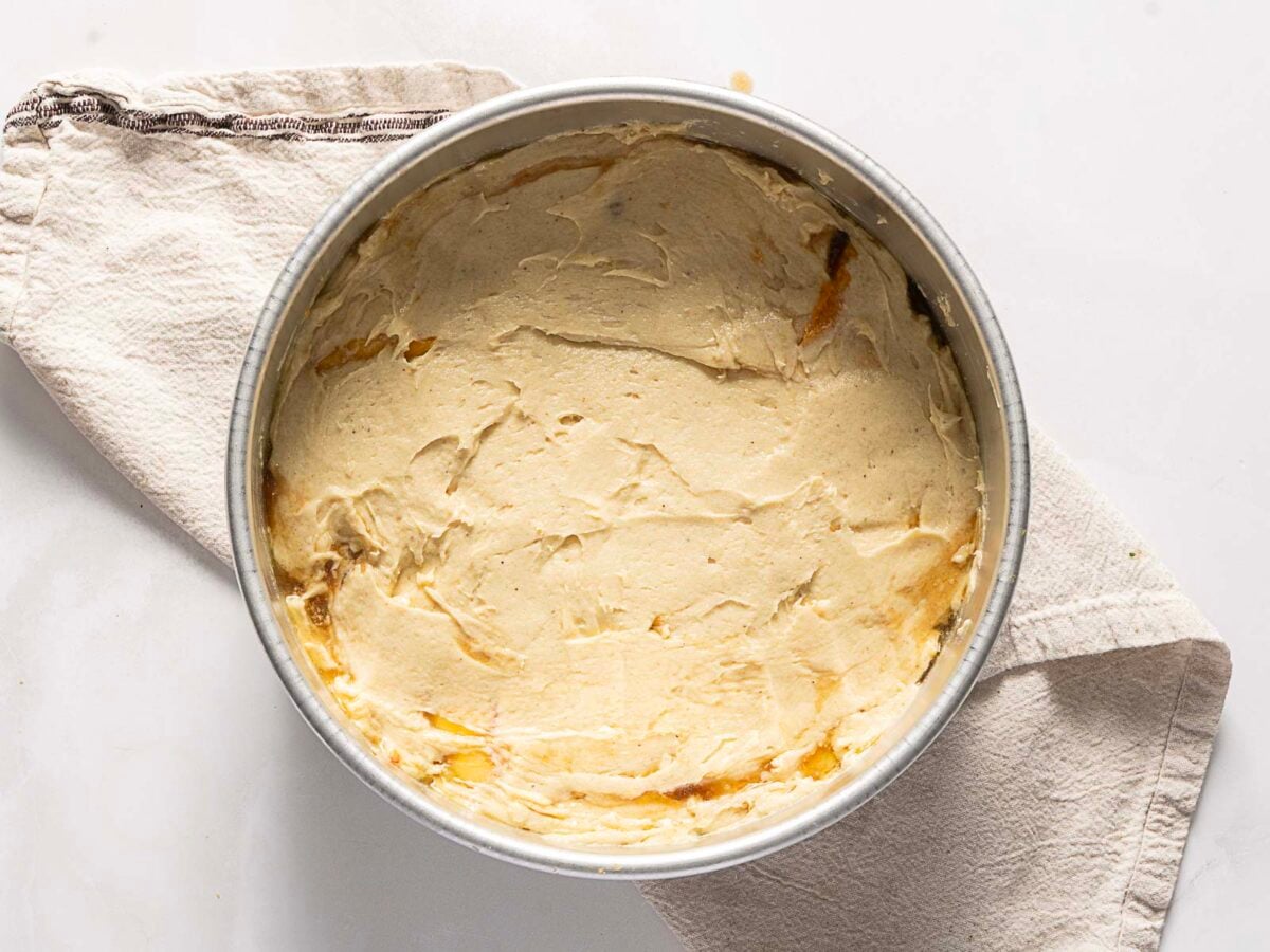 A round baking pan filled with smooth cake batter sits on a beige cloth on a white surface.