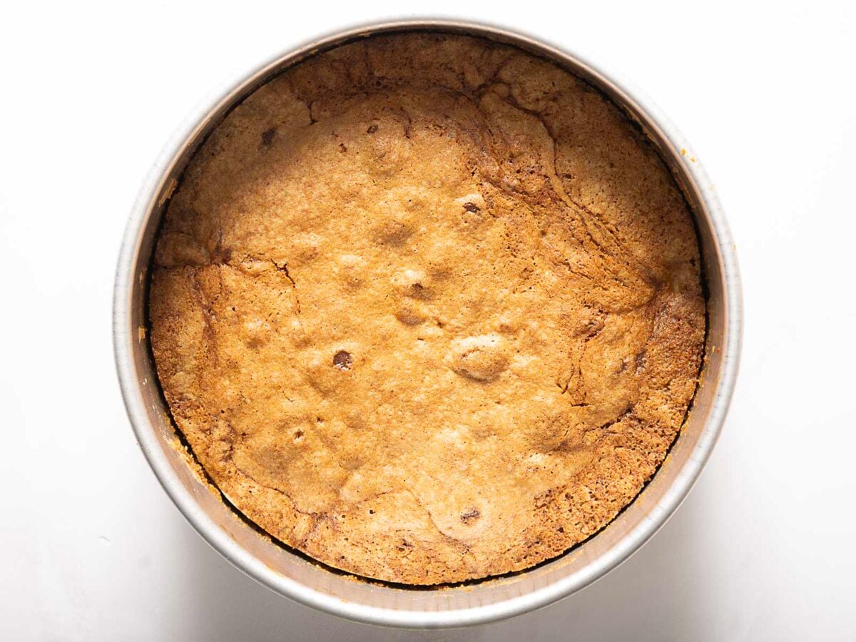 A round, golden-brown cookie baked in a metal pan, viewed from above on a white background.