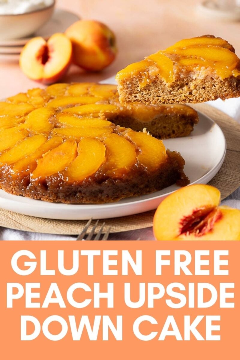 A round upside down cake, made with juicy peaches, is served on a white plate as one slice is being lifted. Fresh peaches are in the background.
