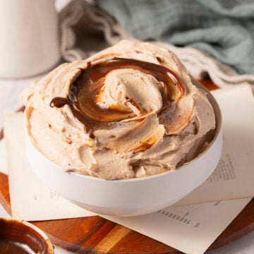 A white bowl filled with whipped chocolate mousse, topped with a swirl of chocolate sauce, sits on top of stacked papers and a wooden board.
