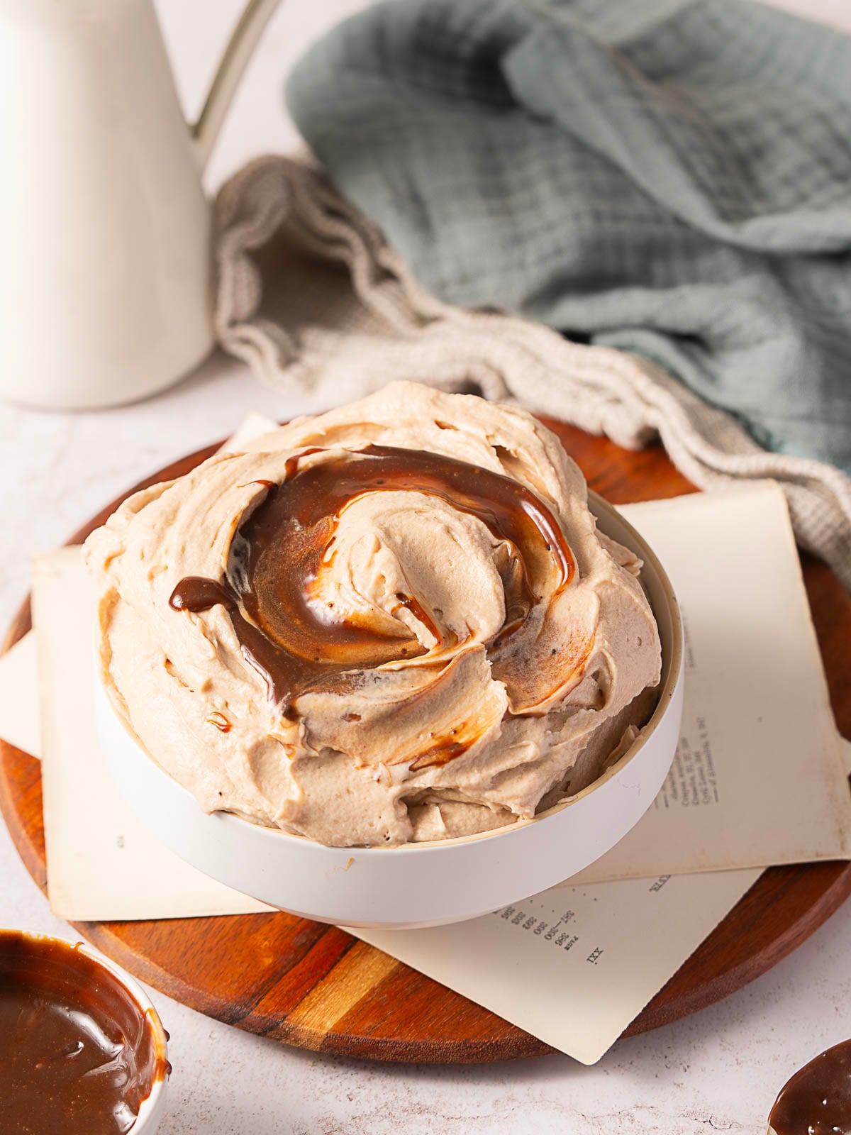 A white bowl filled with swirled chocolate whipped cream sits on a wooden board with papers and a gray cloth nearby.
