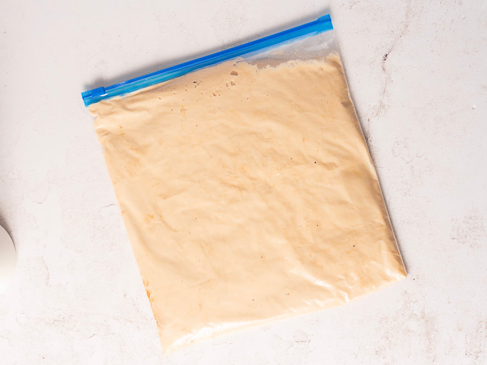 A clear resealable plastic bag filled with a pale beige mixture is placed on a white surface.