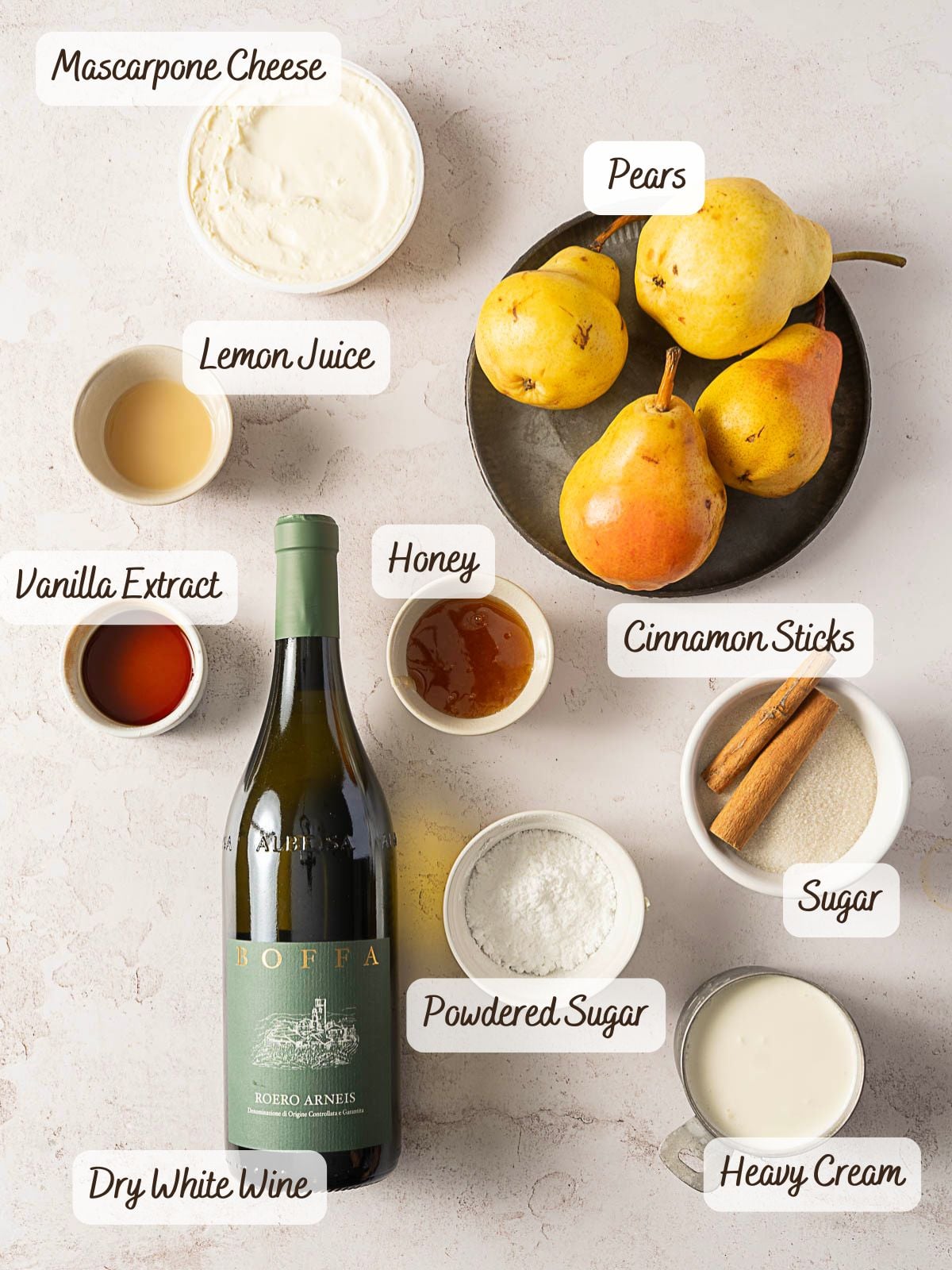 Ingredients for White Wine Poached Pears, including mascarpone cheese, lemon juice, vanilla extract, dry white wine, honey, powdered sugar, pears, cinnamon sticks, sugar, and heavy cream arranged on a light surface.