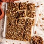 Pecan pie bars cut into squares on parchment paper, with a bowl of whole pecans nearby.